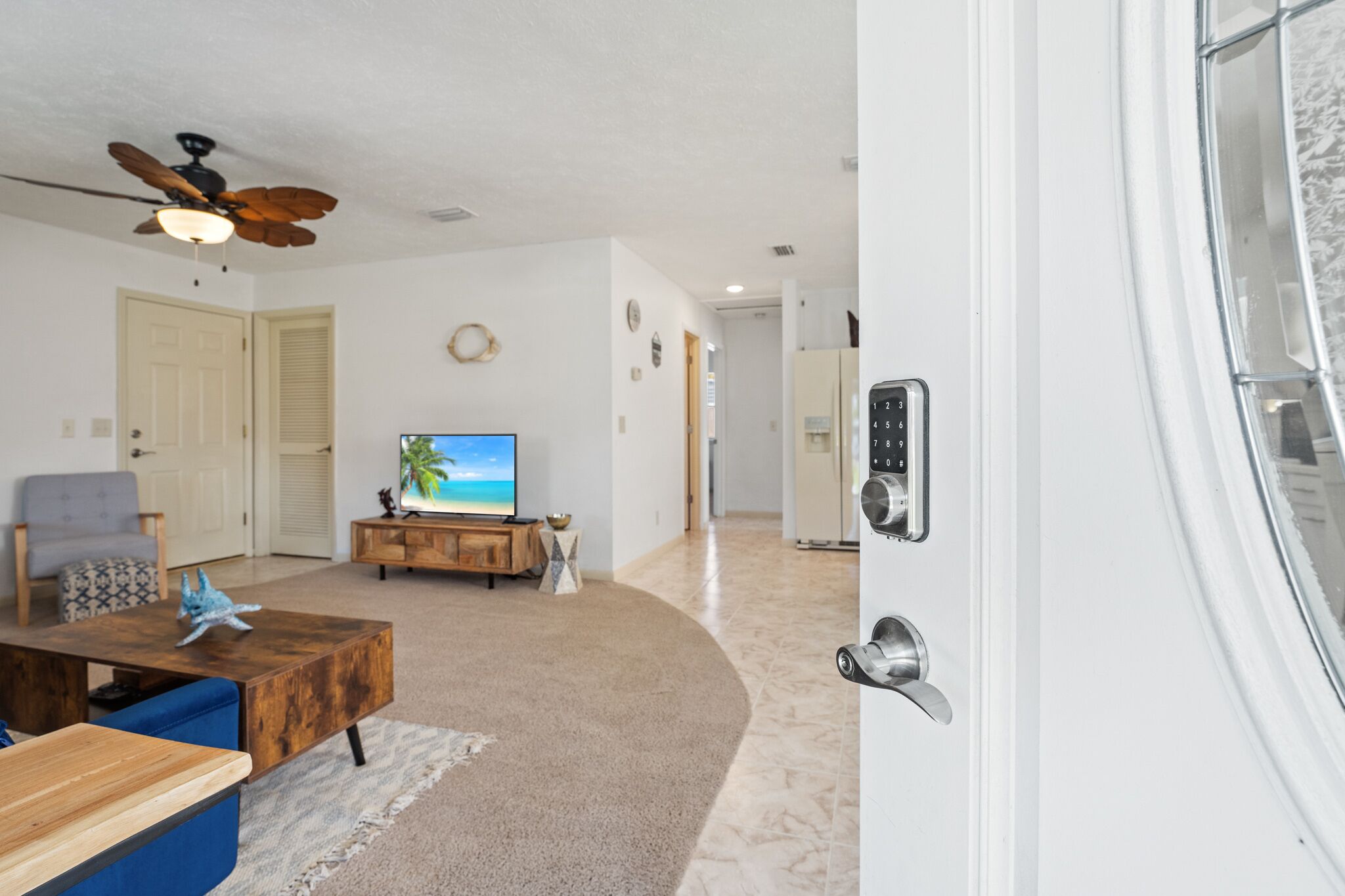 A living room with a television, a ceiling fan, and a door with a keypad lock.