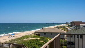 A beach view with a pier extending into the ocean, houses along the shore, and a clear sky.