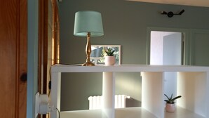 A white console table with a lamp and potted plants, a mirror, and a door in a room with teal walls. - Terrace, Garden, Apartment 80m², mountain view, wifi, office (Bagnères-de-Bigorre)