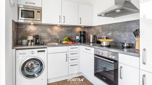 A modern kitchen with white cabinets, a Bosch washing machine, a Bosch oven, and a stainless steel microwave. - Lütte Strandhus - Semi-detached house, fireplace, shower room, washing machine (Olpenitz)