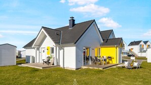 A white house with a grey roof, a yellow garage, and a deck with outdoor furniture. - Lütte Strandhus - Semi-detached house, fireplace, shower room, washing machine (Olpenitz)