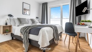 A modern bedroom with a bed, bedside tables, a desk, and a chair. - Lütte Strandhus - Semi-detached house, fireplace, shower room, washing machine (Olpenitz)