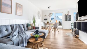 A modern living room with a grey sofa, round wooden tables, and a TV on the right. - Lütte Strandhus - Semi-detached house, fireplace, shower room, washing machine (Olpenitz)