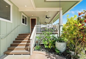 A staircase leading to a porch with a ceiling fan, surrounded by greenery and potted plants.