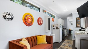 A modern living room with a brown sofa and yellow pillows, a kitchen with white cabinets, and a dining area with a table and chairs. - Container Home w/ a Fenced Yard (Hendersonville)