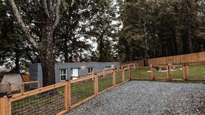 A fenced outdoor area with a gravel path, wooden fence, and a small building with windows. - Container Home w/ a Fenced Yard (Hendersonville)