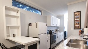 A compact kitchen with white cabinets, a built-in oven, a microwave, and a stainless steel sink. - Container Home w/ a Fenced Yard (Hendersonville)
