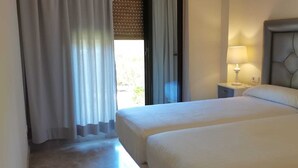 Habitació d'hotel amb dos llits, una tauleta de nit amb una làmpada i una finestra amb cortines.