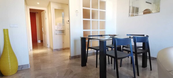A hotel room with a dining area featuring a table and chairs, a large mirror on the wall, and a yellow vase on the floor.