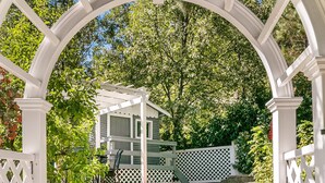 Una pérgola de madera blanca con vistas a una casa y un césped cuidado.