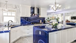 Una cocina moderna con armarios blancos, una isla de mármol azul y una campana extractora de acero inoxidable.