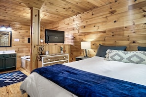 Cozy bedroom with a large bed, bedside table, and television, featuring a sink and window with an outdoor view.