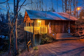 Escape to a secluded cabin surrounded by trees, with a wooden deck and staircase leading to the entrance.