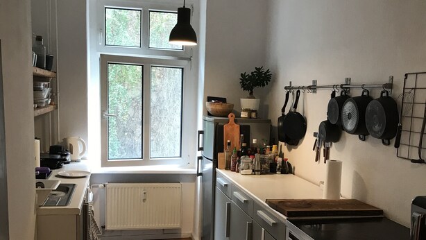 A kitchen with a window, wooden floor, white cabinets, and a hanging pot rack.
