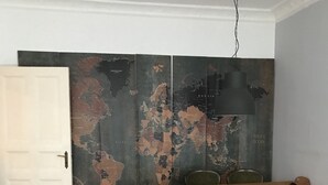 A room with a wooden floor, a grey sofa, a dining table with chairs, and a large world map mural on the wall.
