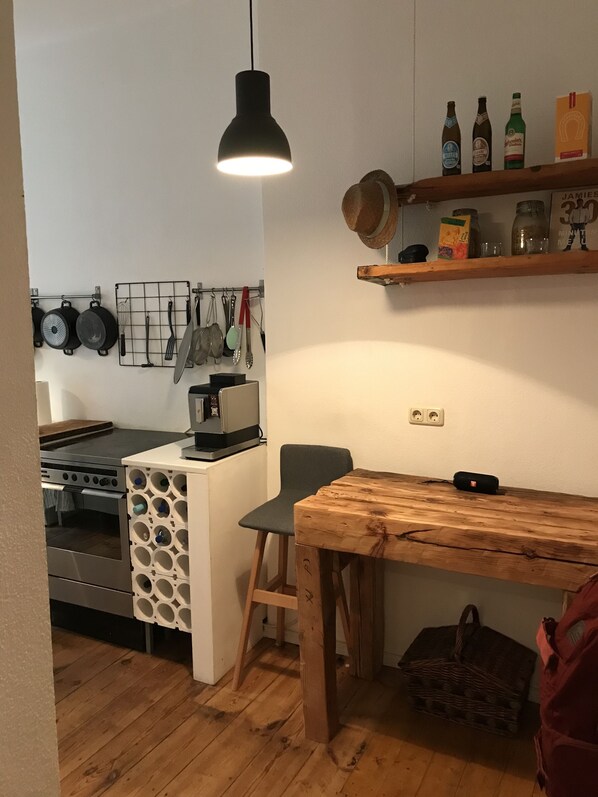 Une cuisine de taille réduite, avec une table en bois, une lampe suspendue et une étagère remplie de bouteilles.