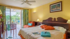 A hotel room with a bed, a ceiling fan, a painting on the wall, and a view of the outdoors through a sliding door. - Charming studio in "Pierre et vacances (Sainte Luce)