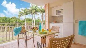 A balcony with a table, chairs, and a view of palm trees. - Charming studio in "Pierre et vacances (Sainte Luce)