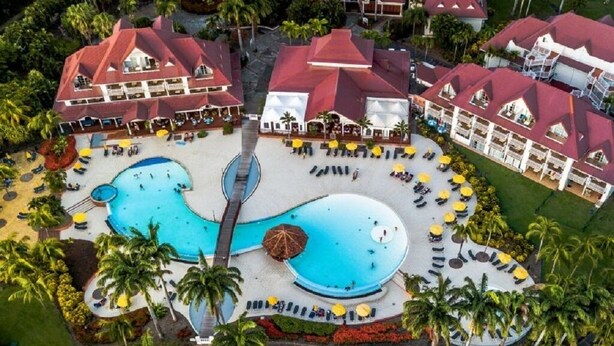 An aerial view of a resort with multiple buildings, a large central pool, and surrounding palm trees. - Charming studio in "Pierre et vacances (Sainte Luce)