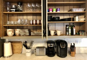Una cocina con estantes de madera que exhiben diversos utensilios de cocina, un tostador, una cafetera y cubiertos.