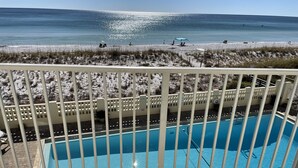 Een zwembad met een witte omheining op de voorgrond, een zandstrand in de achtergrond en een helder uitzicht op de oceaan.