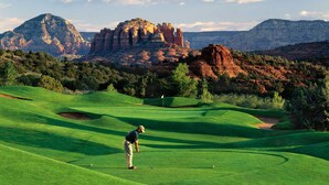 A golf course with a player preparing to hit a ball, surrounded by lush green grass and red rock formations in the background. - Tennis & Pickle ball courts, Golf, Hiking (Sedona)