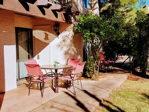 An outdoor patio with a round table and chairs, a small potted plant, and a staircase leading to a covered area.