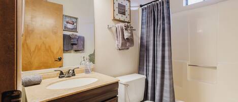 Une salle de bain équipée d’un lavabo, de toilettes et d’une douche. On y trouve un porte-serviettes avec des serviettes et un tableau encadré accroché au mur.