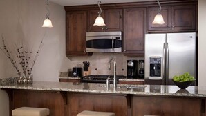 Una cocina con gabinetes de madera oscura, electrodomésticos de acero inoxidable, encimera de granito e iluminación colgante.