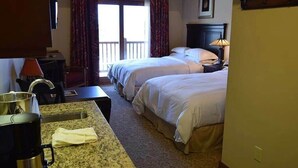 Habitación de hotel con dos camas, un área de cocina con cafetera y un balcón con cortinas.