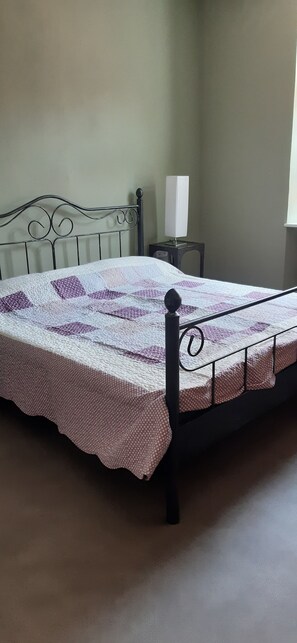 A bed with a quilt, a bedside table with a lamp, and a window.