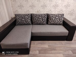 Un canapé modulable recouvert d’un tissu gris, agrémenté de coussins noirs à motifs, le tout placé devant un mur recouvert d’un papier peint à motifs floraux.