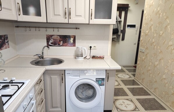 Une cuisine compacte avec des meubles blancs, un lave-linge encastré, une machine à café et une cuisinière à gaz.