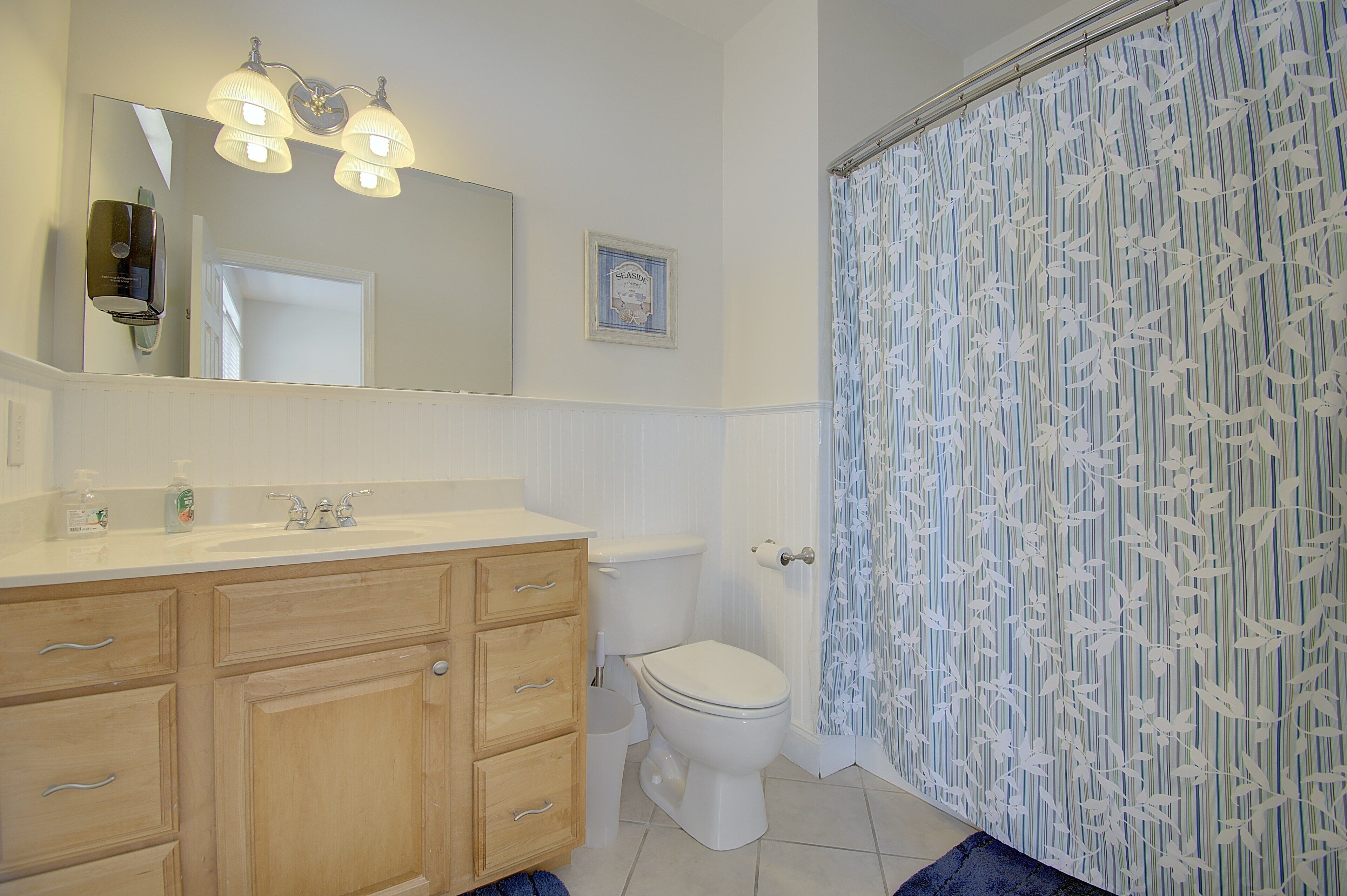 Un baño con tocador de madera, inodoro y cortina de ducha con estampado de hojas.