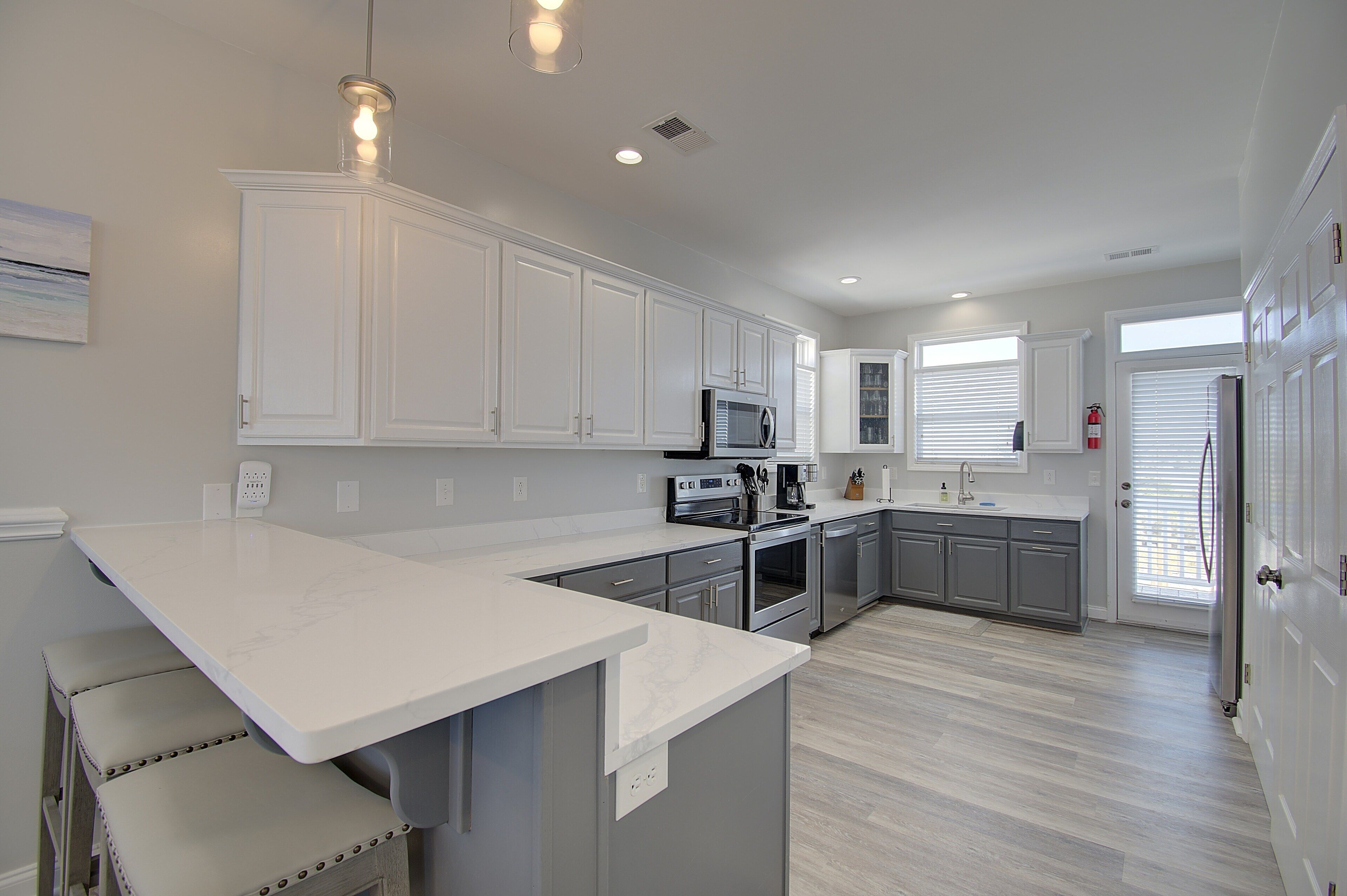 A modern kitchen with white cabinetry, a central island, stainless steel appliances, and a light wood floor.