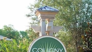 Ein Schild für den Coligny Beach Park mit kreisförmigem Design, montiert auf einem steinernen Sockel mit Dach, umgeben von Grün.