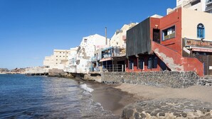 A coastal building with a stone staircase leading to a door, adjacent to a sandy beach.