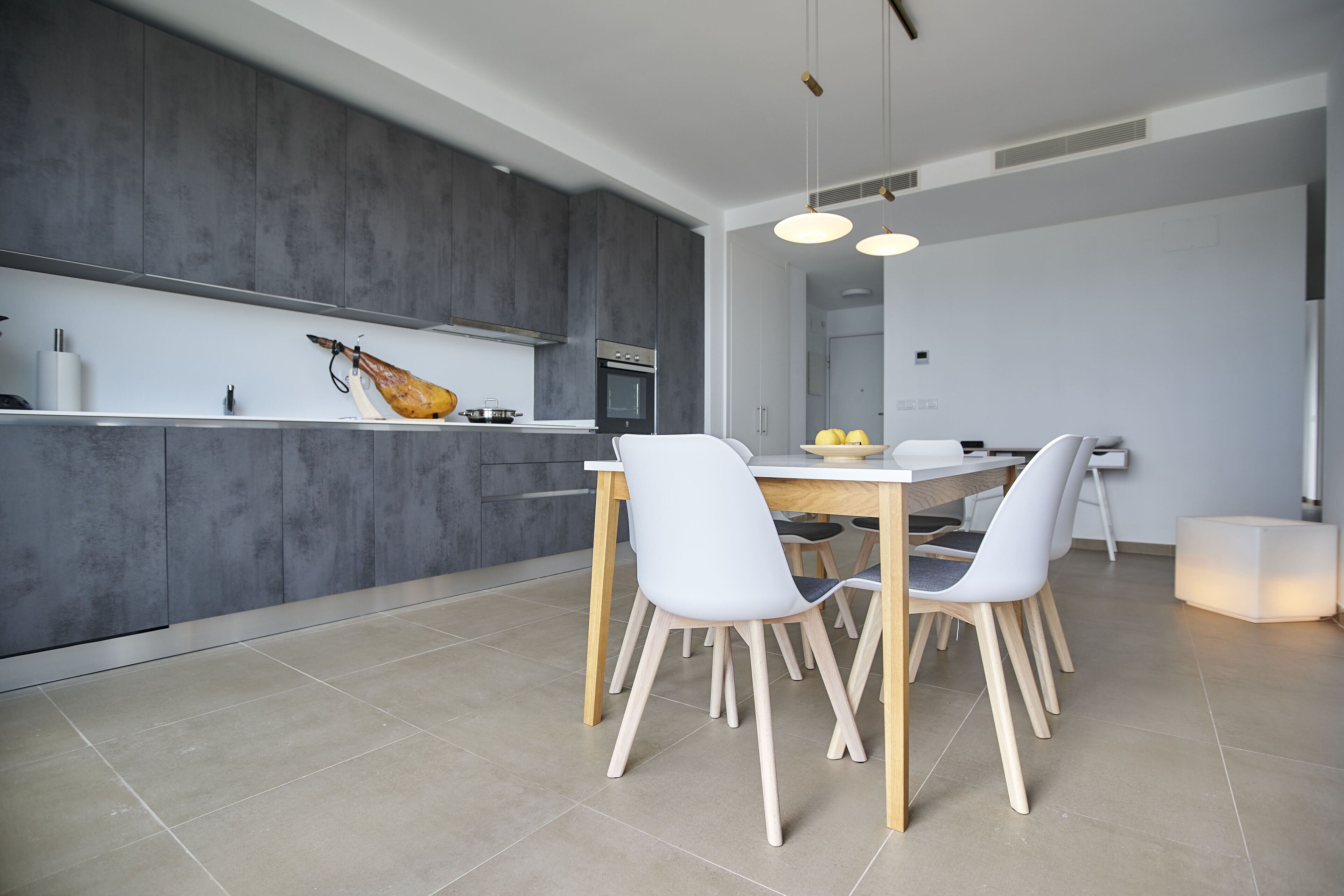 A modern kitchen with grey cabinets, a white countertop, and a dining area with a white table and chairs.