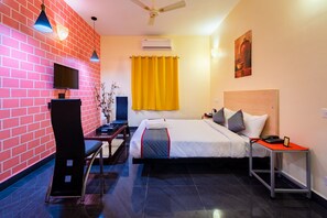 A hotel room with a brick wall, a bed with a headboard, a desk with a chair, a TV, and an air conditioning unit. - Sornalaxmi Residency (Puducherry)