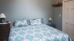 Une chambre à coucher comprenant un lit, deux tables de chevet, une commode, une décoration murale en bois, une étagère avec divers objets et une porte.