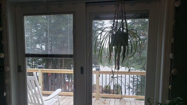 Une terrasse en bois avec une chaise berçante blanche et une plante suspendue.