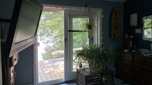 Une pièce dotée d’une porte-fenêtre coulissante donnant sur une terrasse extérieure, d’une commode, d’un miroir et d’une plante suspendue.