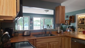 Une cuisine avec des meubles de rangement en bois, une cuisinière noire, un évier et une fenêtre donnant sur un balcon.