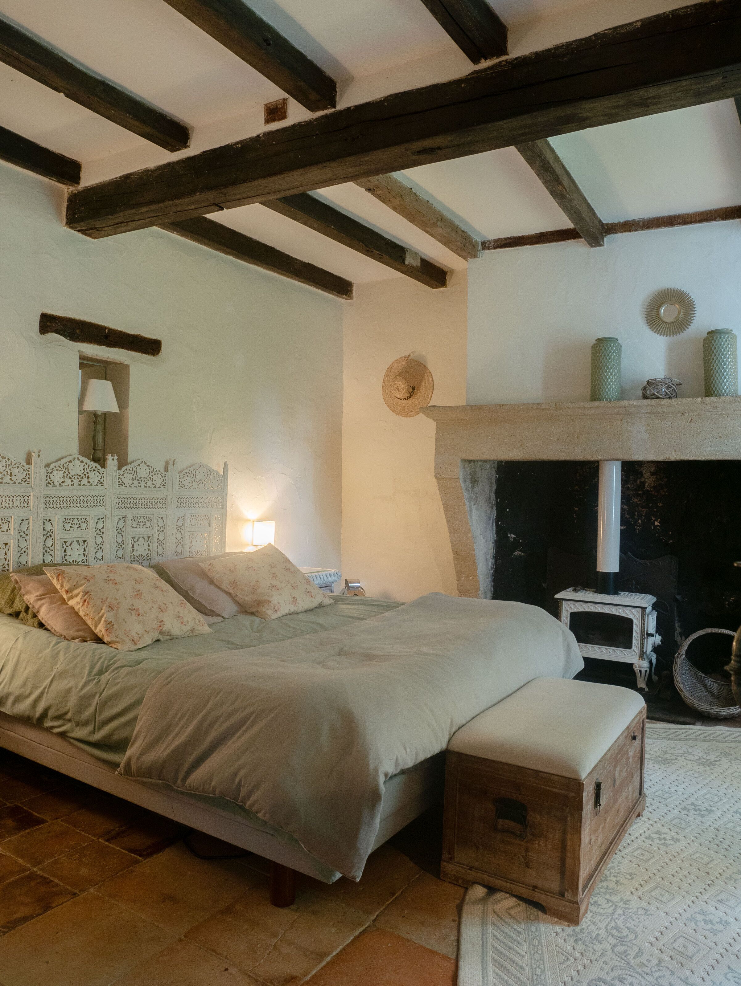 Ein Schlafzimmer mit einem Bett, einem Nachttisch, einer Lampe, einem Kamin und einem gewebten Korb.