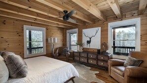A log cabin bedroom with a bed, two armchairs, a dresser, and a deer artwork on the wall. - The Outpost, on Little Pisgah Mountain - a Secluded Modern Cabin Oasis (Hendersonville)