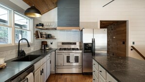 A modern kitchen with a stainless steel stove, refrigerator, and black countertops. - The Outpost, on Little Pisgah Mountain - a Secluded Modern Cabin Oasis (Hendersonville)