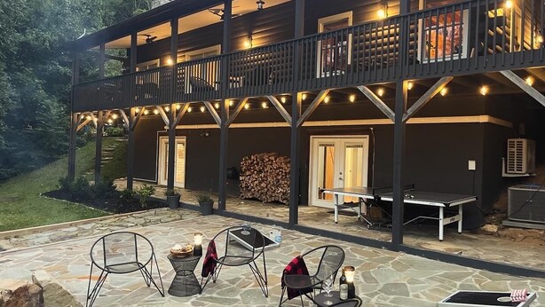 A two-story building with a covered patio area featuring stone flooring, outdoor seating, and a fire pit. - The Outpost, on Little Pisgah Mountain - a Secluded Modern Cabin Oasis (Hendersonville)