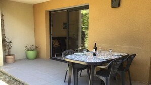 An outdoor patio with a table and chairs, a potted plant, and a sliding glass door leading to an interior space.