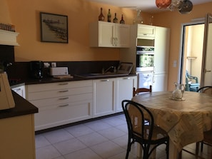 Cozinha com armários brancos, uma mesa de jantar com cadeiras e uma janela com vista para o verde.