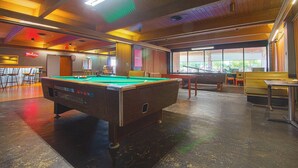 Uma mesa de bilhar em um ambiente com tetos de madeira e janelas amplas.